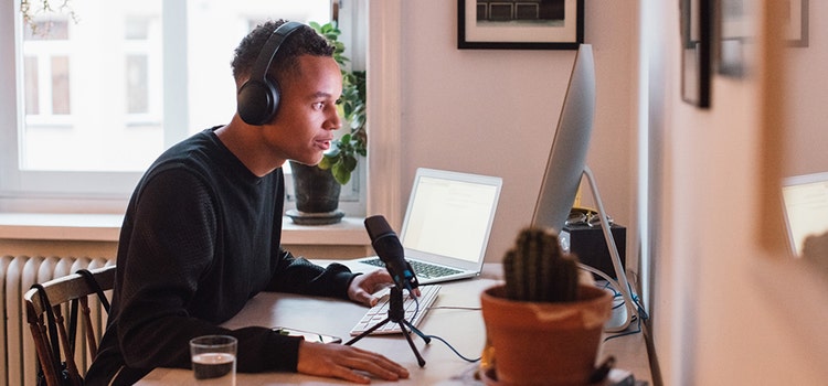 https://www.adobe.com/products/audition.html | Person mit Kopfhörern arbeitet an einem Computer mit Mikrofon in einem Home-Studio.