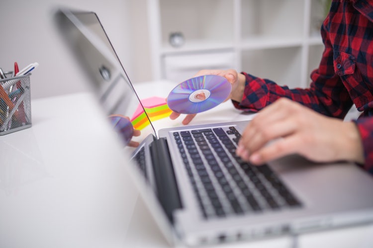Eine Frau legt eine DVD ins DVD-Fach ihres Notebooks ein.