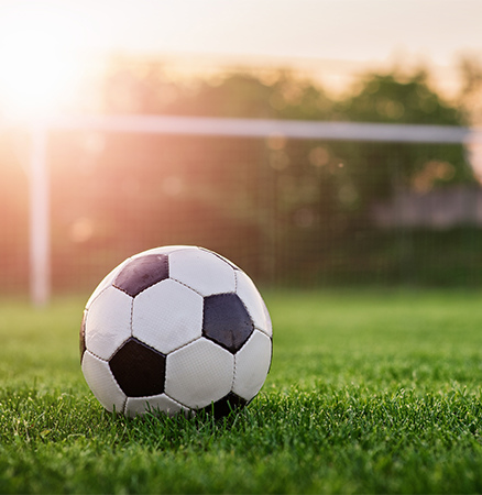 Fußball auf Rasen mit Tor im Hintergrund