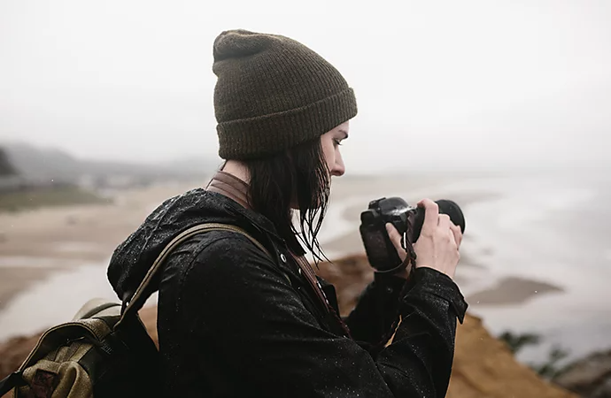 Bild einer Fotografin, die an einer Küste steht und auf ihre DSLR-Kamera blickt