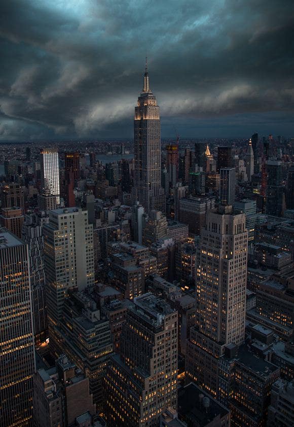 Das Empire State Building ragt zwischen kleineren Gebäuden in einem dunkelgrauen Stadtpanorama empor