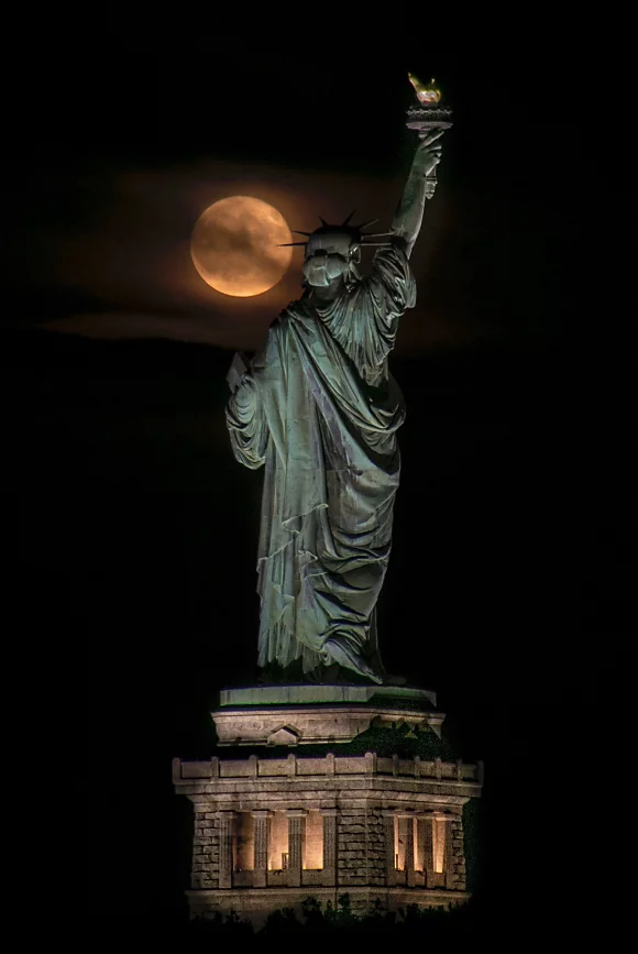Ein Vollmond, der teilweise von Wolken verdeckt wird, über der linken Schulter der Freiheitsstatue