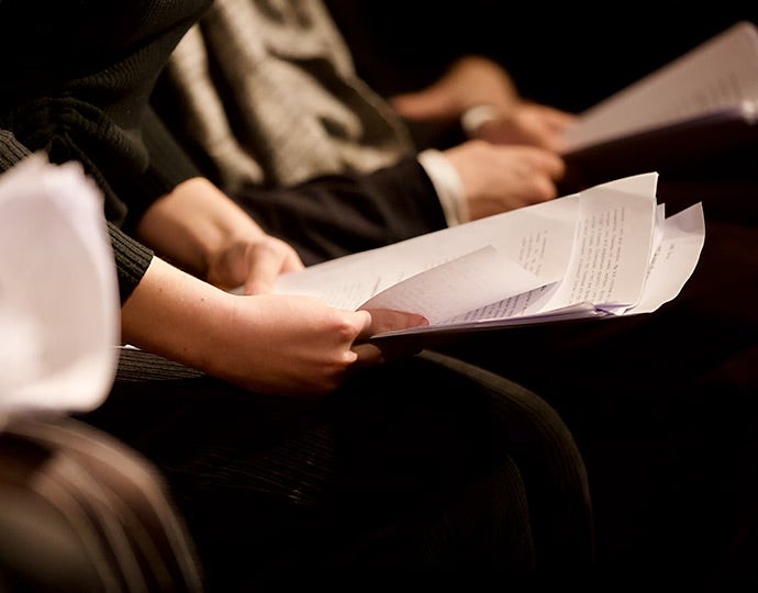 Blick auf mehrere Personen, die in einer Reihe sitzen und Drehbücher in der Hand halten