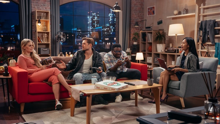 Standbild aus einer Sitcom: Freunde sitzen gemeinsam im Wohnzimmer auf dem Sofa