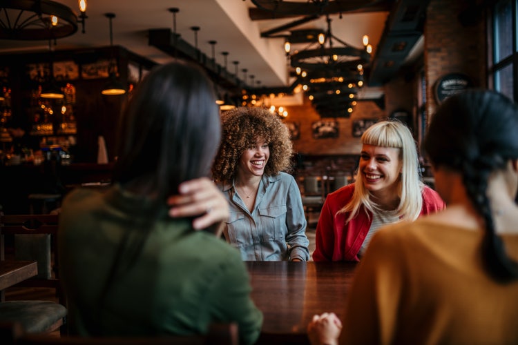 Over-the-shoulder-Shot mit zwei Frauen im Off im Vordergrund und mit Fokus auf zwei weitere Frauen im On in der Mitte