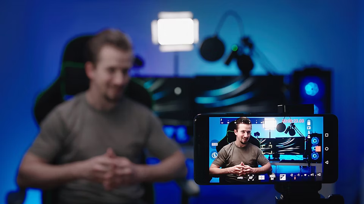 Ein junger Mann spricht zu seinen Followern. Im Vordergrund ist ein Smartphone abgebildet, mit dem der Livestream aufgenommen wird.
