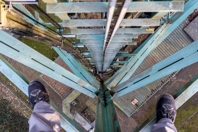 Füße auf zwei Streben einer Leiter beim Aufstieg auf einen Turm mit Blick nach unten