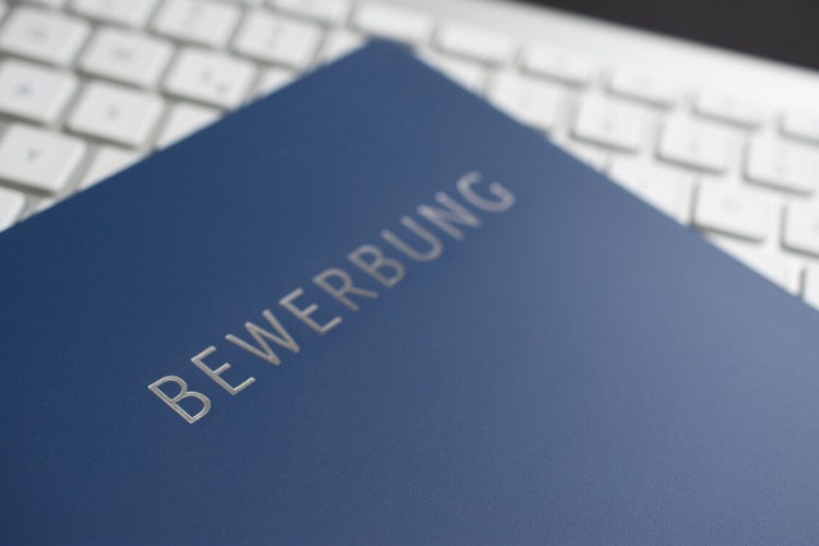 Image of a blue book over a laptop keyboard. The book is titled "Bewerbung"