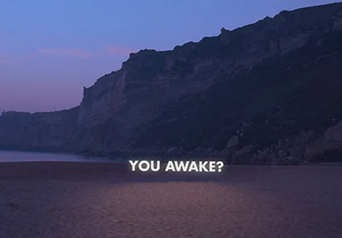 Die Wörter „YOU AWAKE?" über einem dunklen Strandhintergrund