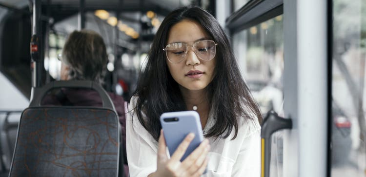 En person med briller sidder i en bus og kigger på en mobilenhed