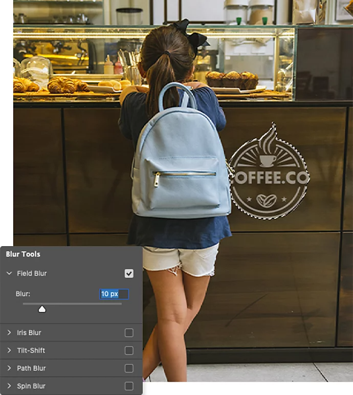 Indstillingsvinduet for Sløringsværktøjet i Adobe Photoshop vist hen over et foto af et barn foran en disk med en kaffebars logo