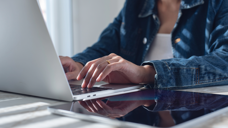 A woman wearing a dark denim shirt, visible from the neck down only, types on a laptop