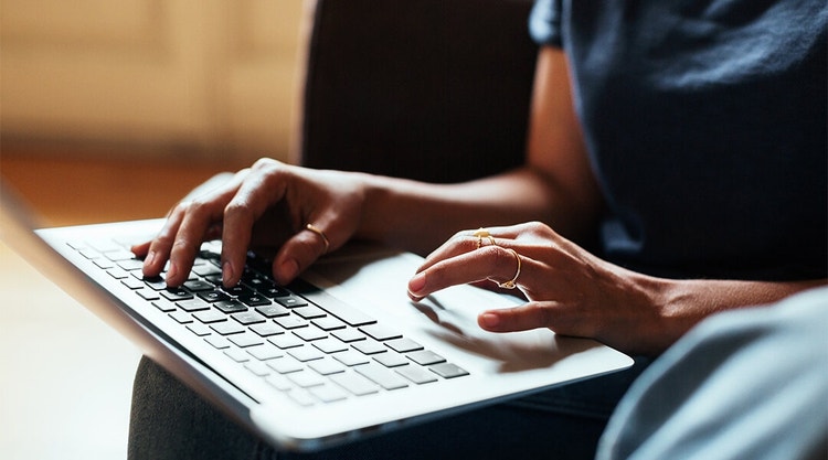 Close-up of a woman's fingers with gold rings on them using a laptop to create an NDA.
