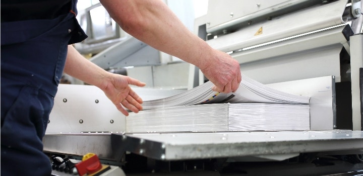 El gráfico muestra a una persona examinando una pila de papel en una imprenta.