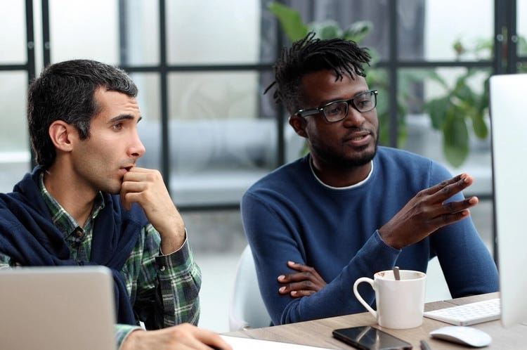 La imagen muestra a dos hombres hablando por la computadora en la oficina.