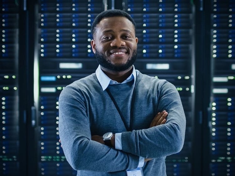 For administrators Deploy Adobe Express for schools and school districtsA person smiling with crossed arms standing in front of a server room.