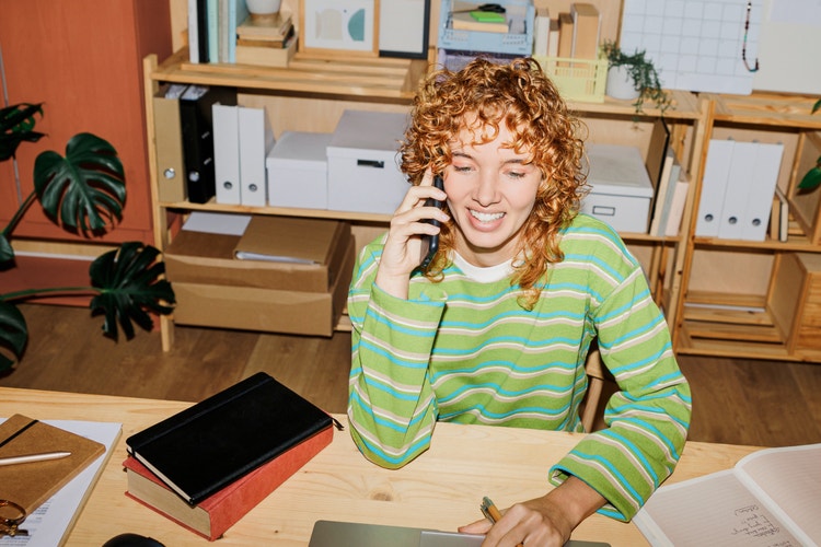 woman in a green long-sleeved shirt at a desk with bookshelves behind her