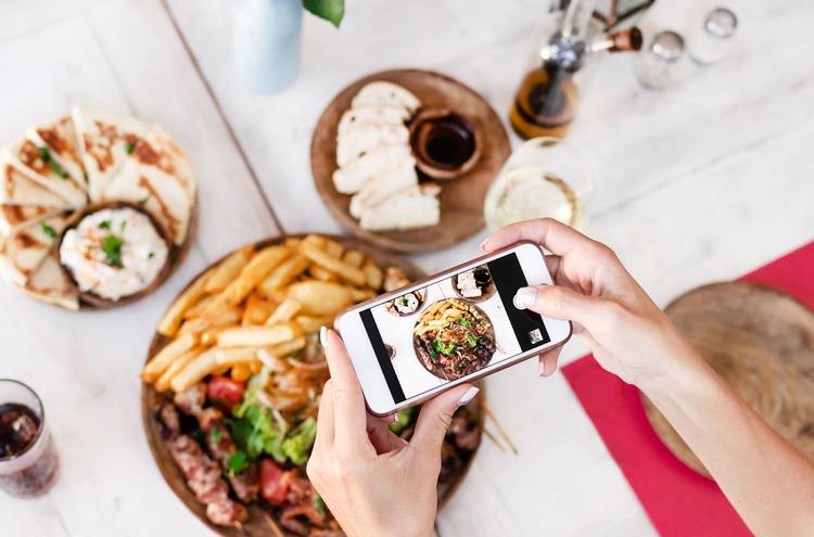 Instagrammer taking an aerial view picture with their iPhone of uneaten dishes at a restaurant