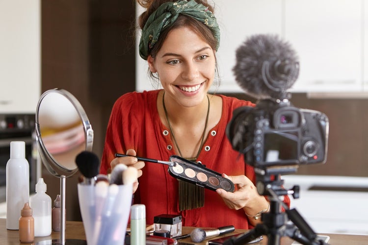 A vlogger recording a makeup tutorial into a camera with a mic