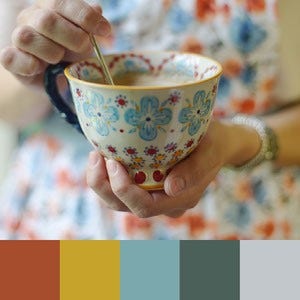 A color palette created from an image of a close up of a hand holding a blue, red, yellow, and white teacup