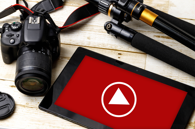 A tablet with a YouTube play button next to a camera and a tripod