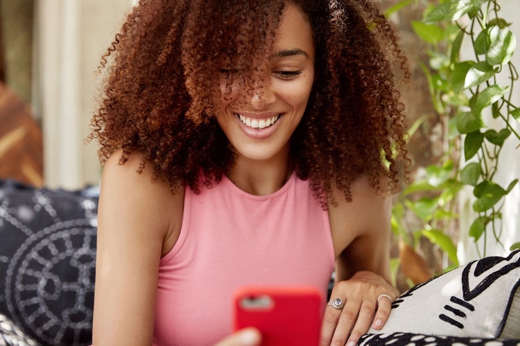 A person with curly hair looking down at a phone and smiling
