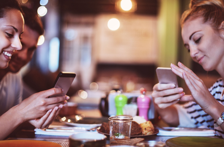 phones at table A group of three people sit at a table in a restaurant or cafe. Two of them are scrolling on their phones.