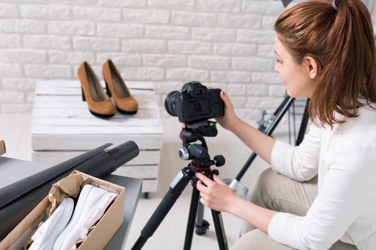 A Facebook Marketplace seller taking a product photo of a pair of brown heeled shoes with a camera and tripod.