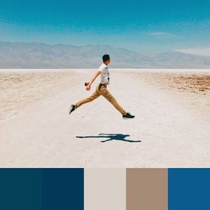 A color palette created from an image of a person jumping over a dirt road with blue sky and mountains in the distance