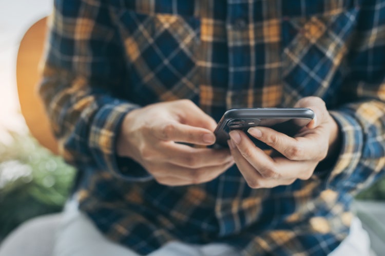 Man in a yellow and blue flannel typing on a smartphone