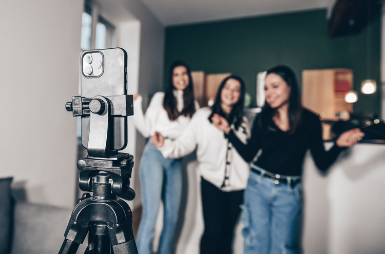 Filming a TikTok Three women pose in front of a mobile phone that is held on a tripod.