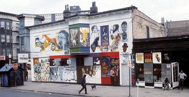 A street in 1960's Chicago with a building at center featuring the protraits of important Black historical figures. Several people are variously walking or sitting down on the sidewalk.