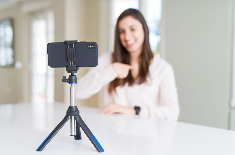 Filming a Reel A phone, held by a tripod, sits on a desk in front of a woman who is pointing to herself.