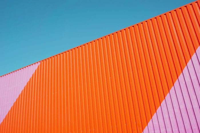 Orange and pink colorful corrugated surface. Above, there is a clear blue sky.