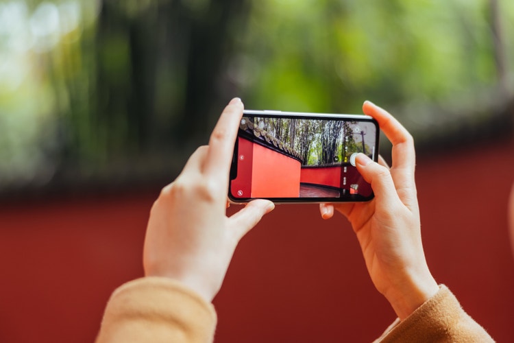 hands holding a smartphone taking a photo of a forest with red buildings