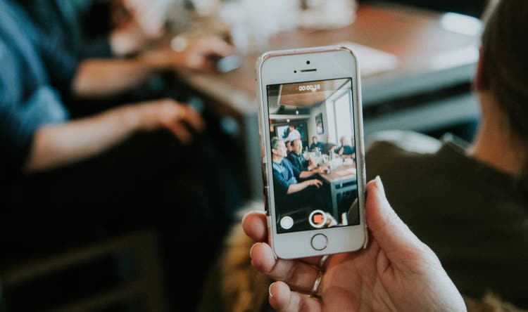 A hand holding a smartphone that is recording a business meeting.