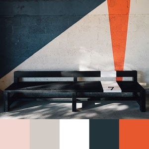 A color palette created from an image of a black and white bench against a white, orange, and navy blue wall