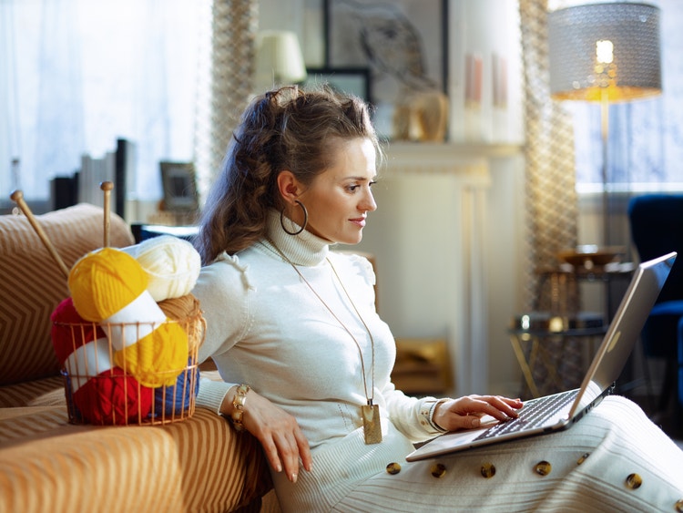 digital business: Woman watching on her laptop with yarn and needle