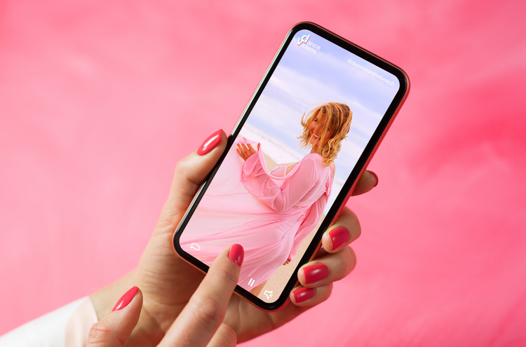 Phone TikTok A hand holds a mobile phone in shot, playing a video of a woman in a pink dress.