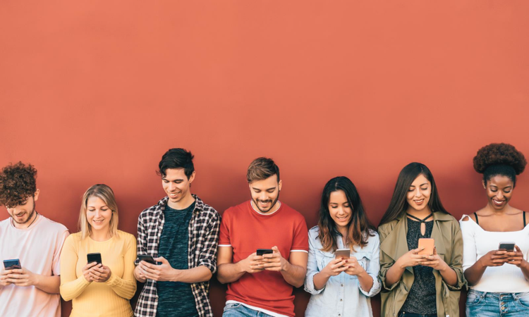A group of smiling 20-somethings standing shoulder to shoulder but are only engaging with their phones. Orange background