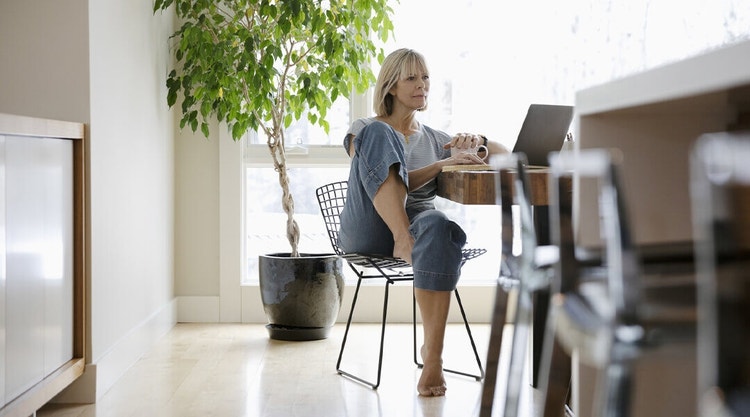 Blonde woman wearing jeans reviewing a business contract on a laptop while sitting at a table