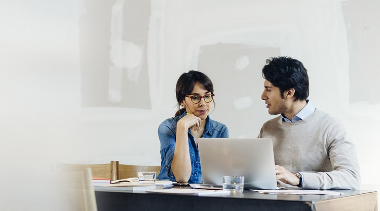 A property owner and property manager reviewing a property management agreement on a laptop together
