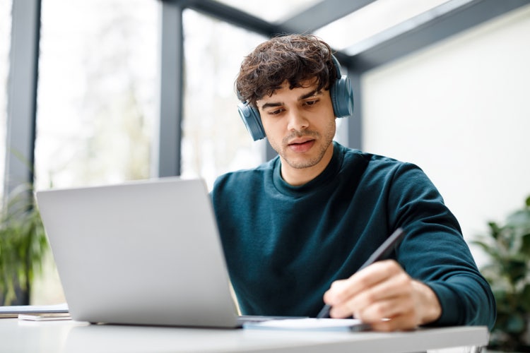 Jeune étudiant prenant des notes devant son ordinateur portable pour son mémoire de fin de d'études.