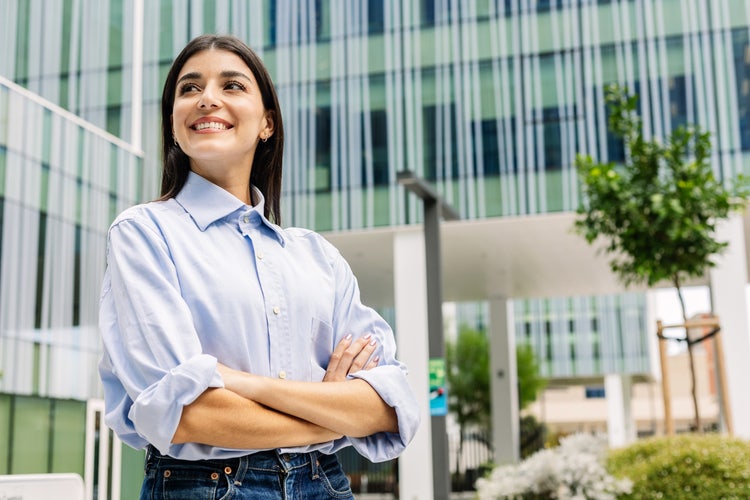 Une jeune femme sourit avec assurance et a les bras croisés.