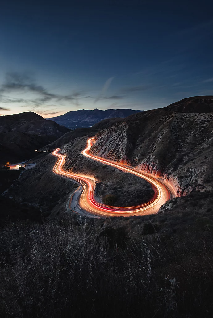 Traînées lumineuses laissées par une voiture en mouvement sur une route à flanc de colline