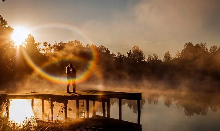 Couple s’embrassant, debout sur le ponton d’un lac, sous les feux d’un halo