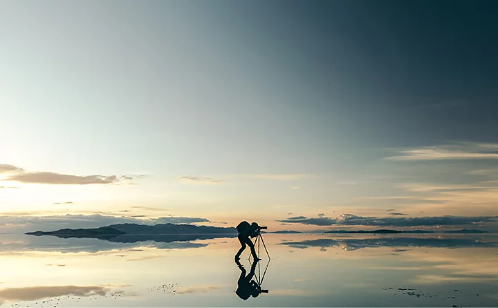Photographe prenant une photo avec son appareil posé sur un trépied debout dans une eau très peu profonde