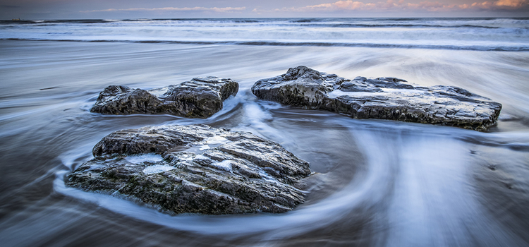 Flou de mouvement de l’eau s’écoulant sur des rochers au bord du rivage
