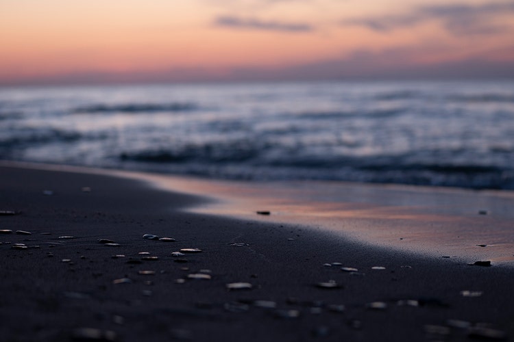 Vue anamorphique d’une plage au coucher du soleil, avec les rochers nets au premier plan et le coucher de soleil ainsi que la mer flous à l’arrière-plan