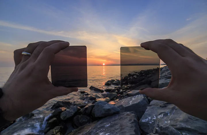 Personne tenant deux filtres&nbsp;ND différents devant un lever de soleil